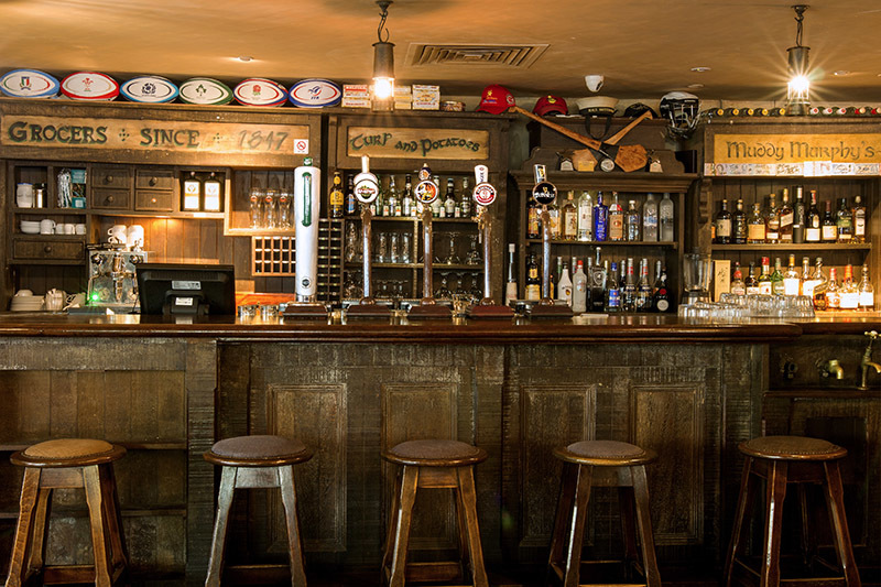 The warmly lit wooden bar at Muddy Murphy’s, with traditional Irish signs and empty bar stools